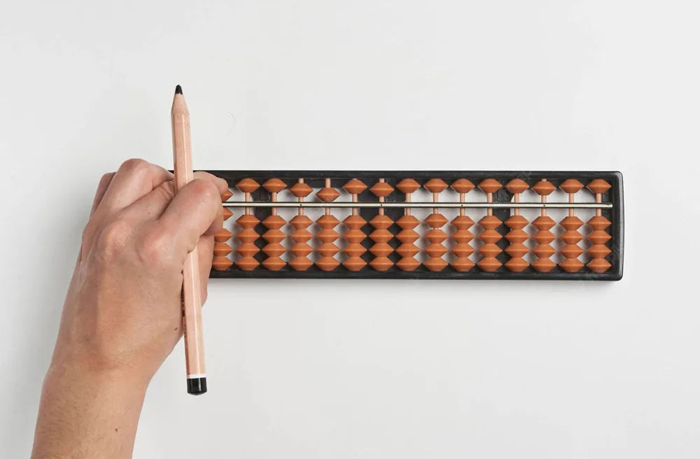 Hand using a soroban abacus with a pencil for arithmetic practice